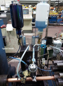 Close-up of a hydraulic lubrication system with two fluid containers and various connected tubes in an industrial setting.