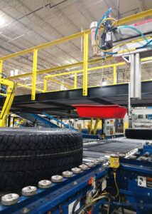 Automated assembly line featuring conveyor belts, tires, and a red tool tray in a modern manufacturing facility.