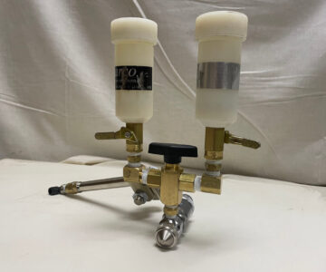 Two-chamber fluid dispenser with brass valves and clear containers on a white background.