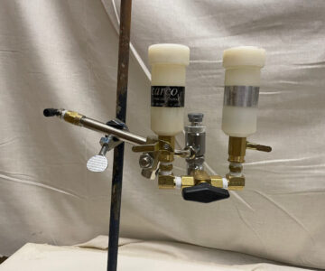 Dual-liquid dispenser with nozzles and levers, used for precise chemical mixing, set against a white backdrop.